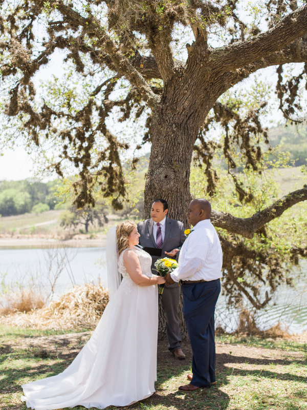 Everlasting Elopements couple holding hands during ceremony in front of a big tree and lake at Joshua Springs